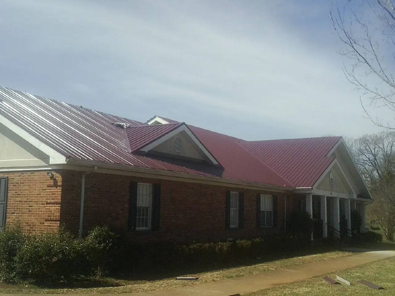 Red metal roof with gabled entries on a long brick building, from a Hail Damage Roof Repair job in Onset