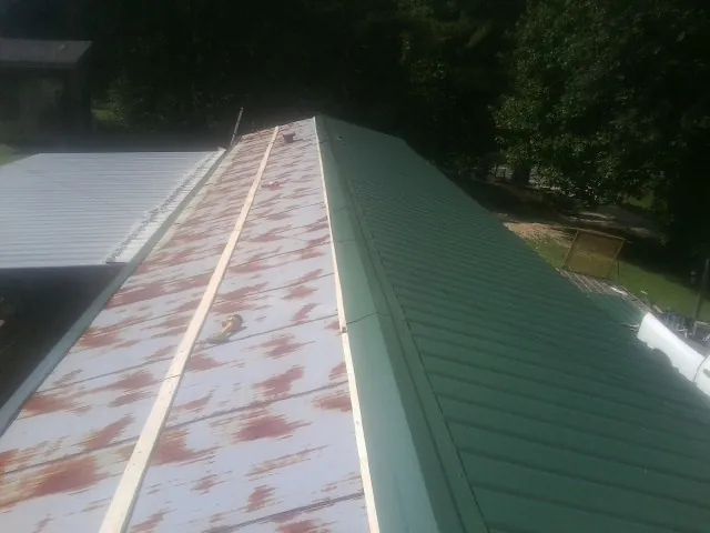 Old rusted panels beside newly installed green metal roofing — Wind Damage Roof Repair by Roofing Brothers in Onset