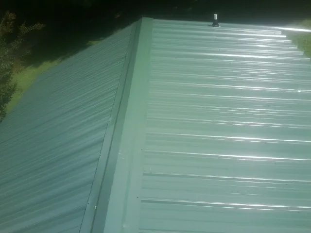 New green metal panels meeting at the ridge of a roof — Flat Roof Repair work by our crew in Onset